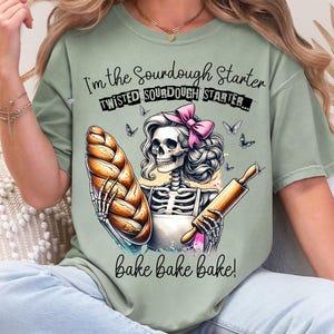 Puede incluir: Una camiseta verde con un esqueleto sosteniendo una hogaza de pan y un rodillo. El texto en la camiseta dice "I'm the sourdough starter, twisted sourdough starter... bake bake bake!"