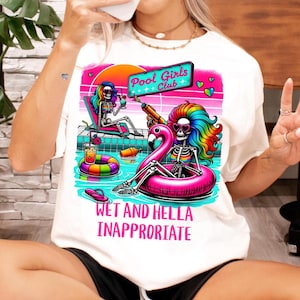 Op de afbeelding: Wit T-shirt met een kleurrijke afbeelding van skeletfiguren op een zwembadfeest. Het ontwerp bevat een flamingo-drijver, cocktails en de tekst "Pool Girls Club" en "Wet and Hella Inappropriate."
