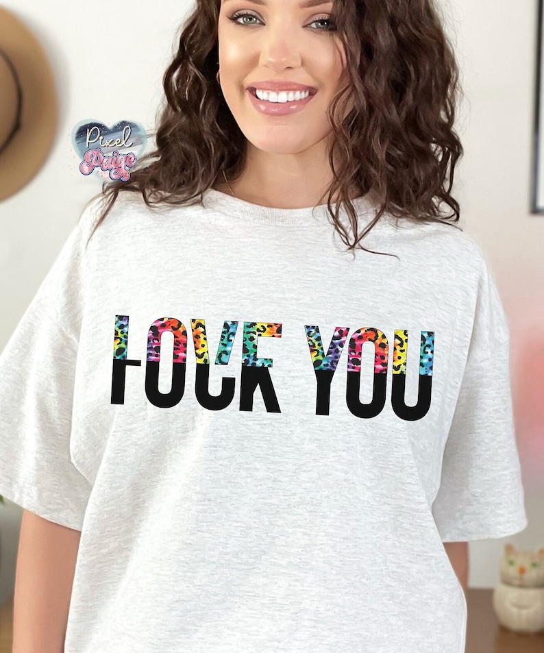 K&ouml;nnte beinhalten: Ein graues T-Shirt mit dem Aufdruck "LOVE YOU" in schwarzen Buchstaben. Die Buchstaben sind mit einem Regenbogen-Leopardenmuster umrandet.