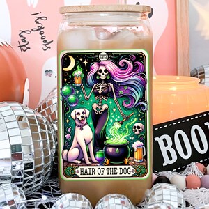 May include: A glass jar with a wooden lid and a colorful sticker featuring a skeleton with purple and blue hair holding a beer mug. The sticker says "Hair of the Dog" and has a green cauldron with a dog beside it.