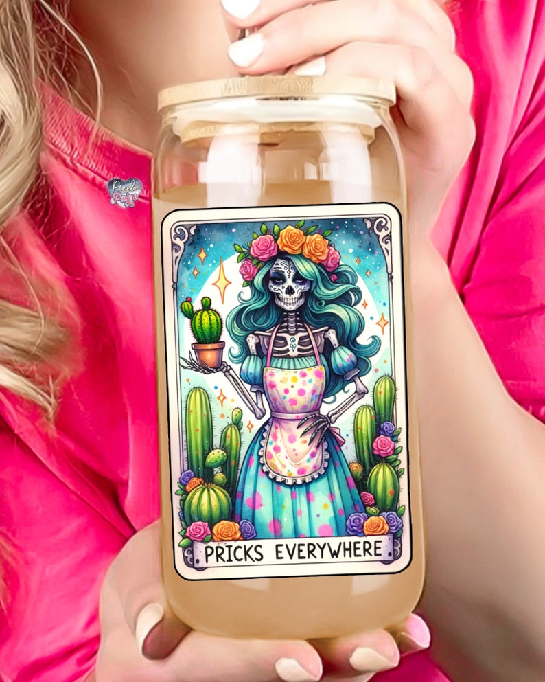 Puede incluir: Un tarro de vidrio con tapa de madera y una ilustraci&oacute;n colorida de un esqueleto con una corona de flores y un delantal de lunares que sostiene un cactus. El texto "Pricks Everywhere" est&aacute; impreso debajo de la ilustraci&oacute;n.
