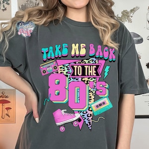 May include: A gray t-shirt with the text "Take Me Back To The 80's" in a colorful retro design. The design includes a boombox, roller skates, and a cassette tape.
