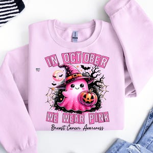 Peut inclure: Sweat-shirt rose avec un fant&ocirc;me portant un chapeau de sorci&egrave;re et tenant une citrouille. Le texte "In October We Wear Pink" et "Breast Cancer Awareness" est imprim&eacute; sur le sweat-shirt.