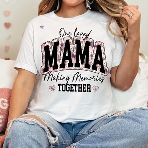 May include: White t-shirt with a floral design and the text "One loved MAMA Making Memories TOGETHER" in black.