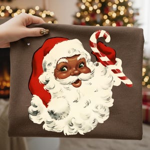 May include: A brown fabric item featuring a vintage illustration of Santa Claus with a red hat and a white beard, holding a red and white candy cane. The Santa has a smiling expression and is set against a brown background. Christmas themed.