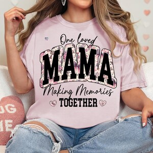 May include: Pink t-shirt with a floral print design. The shirt has black text that reads "One loved MAMA Making Memories TOGETHER".