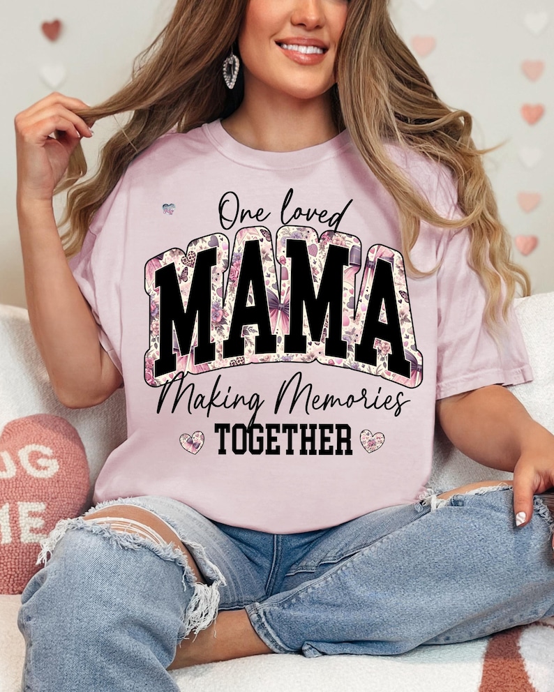 May include: Pink t-shirt with a floral print design. The shirt has black text that reads "One loved MAMA Making Memories TOGETHER".