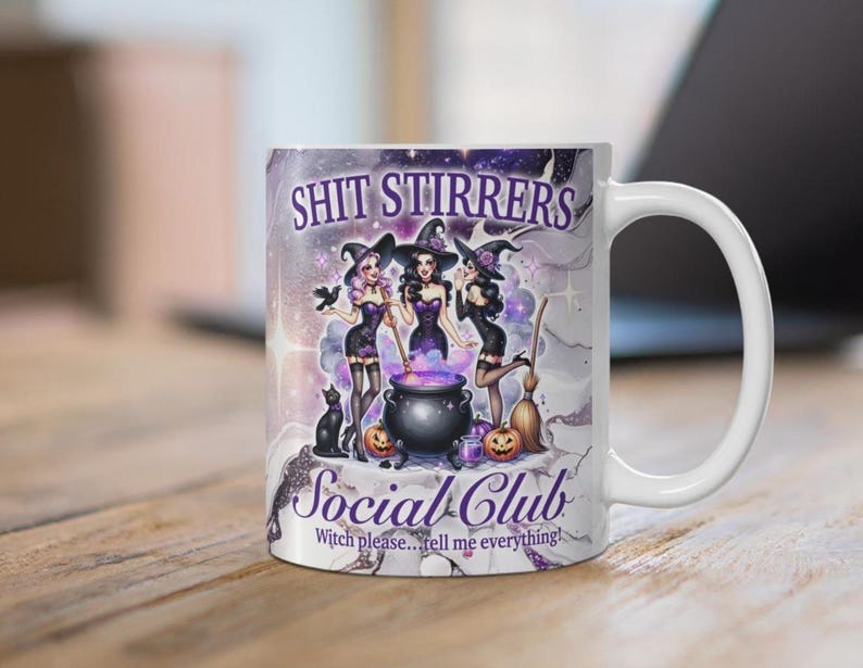 Op de afbeelding: Witte keramische mok met een paars, zwart en wit ontwerp met drie heksen met een ketel en de tekst "Shit Stirrers Social Club Witch please...tell me everything!"