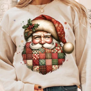 May include: A cream-colored sweatshirt featuring a detailed illustration of Santa Claus. Santa's face is framed by a red and white fur-trimmed hat and a patchwork beard in shades of red, green, and brown. A sprig of holly adorns the hat.