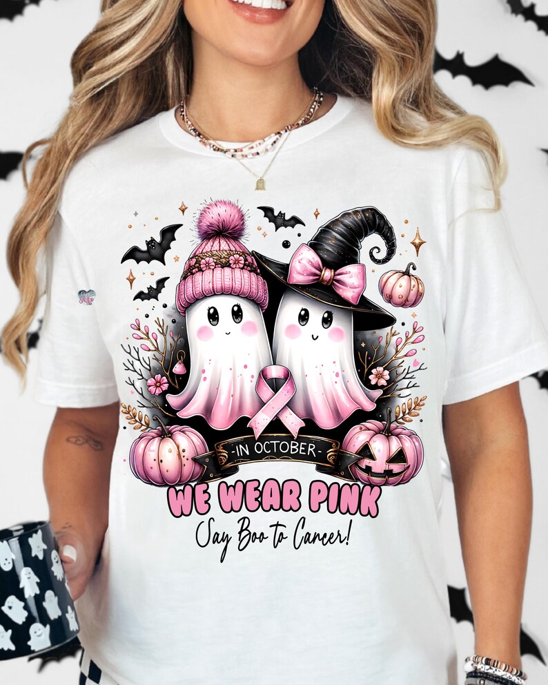 Puede incluir: Camiseta blanca con una cinta rosa, dos fantasmas con sombreros de bruja y calabazas. El texto dice "En octubre, usamos rosa, &iexcl;Digamos Boo al c&aacute;ncer!"