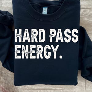 May include: A navy blue sweatshirt with the words "HARD PASS ENERGY" printed in large, distressed white letters. The sweatshirt is a crew neck style.