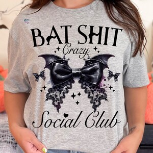 May include: Gray t-shirt with a black bat design and the text "Bat Shit Crazy Social Club".