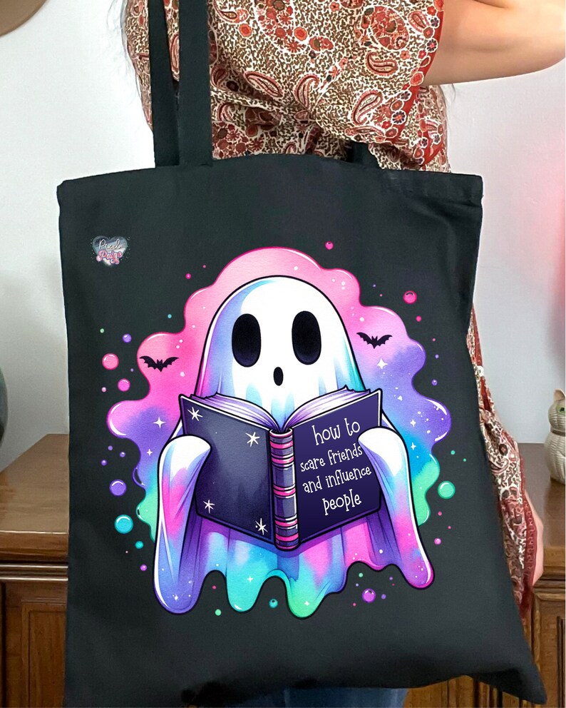 May include: A black tote bag with a ghost holding a book that says "how to scare friends and influence people". The ghost is surrounded by a pink, blue, and green glow.