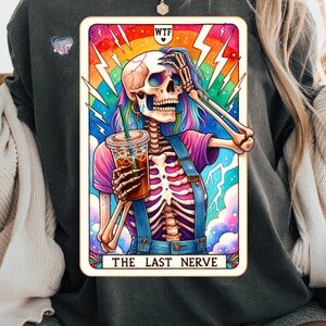 K&ouml;nnte beinhalten: Eine Tarotkarte mit einem Skelett, das eine Tasse Kaffee h&auml;lt. Die Karte tr&auml;gt den Titel "The Last Nerve" und hat die Buchstaben "WTF" in der oberen Ecke. Die Karte ist mit einem Regenbogenhintergrund und Blitzen illustriert.