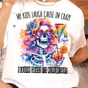 May include: White t-shirt with a colorful skeleton graphic and the text "My kids laugh cause I'm crazy I laugh cause it's hereditary".