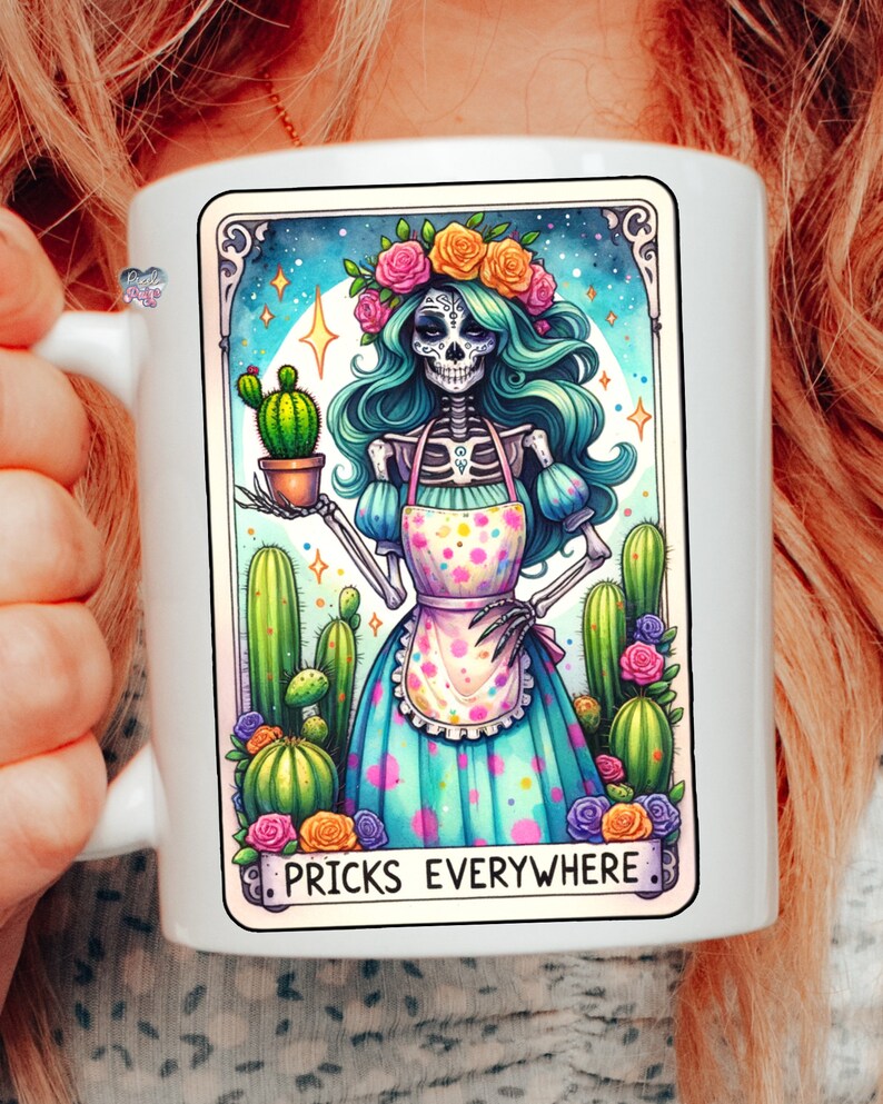 Puede incluir: Taza de cer&aacute;mica blanca con una ilustraci&oacute;n colorida de un esqueleto con una corona de flores y un vestido azul con lunares blancos. El esqueleto sostiene un cactus en maceta y el texto "Pricks Everywhere" est&aacute; impreso debajo de la imagen.