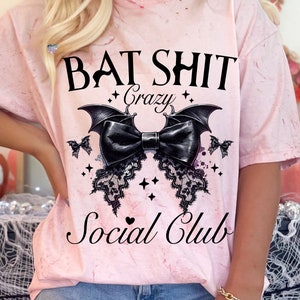 May include: Pink tie-dye t-shirt with a black bat and bow graphic. The text "Bat Shit Crazy Social Club" is printed on the shirt.