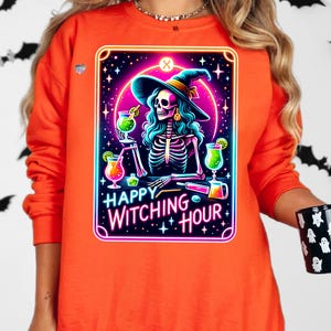 Pu&ograve; includere: Felpa arancione con una grafica di una strega scheletro che indossa un cappello da strega e tiene un cocktail. La grafica &egrave; in stile neon con il testo "Happy Witching Hour".
