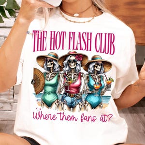May include: White t-shirt with a graphic of three skeletons wearing sunglasses and hats, holding drinks. The text "The Hot Flash Club" and "Where them fans at?" is printed on the shirt.