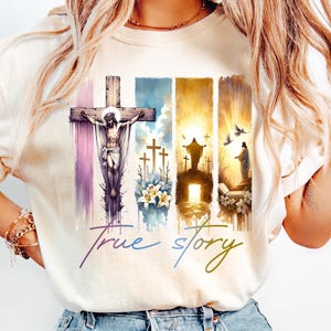 May include: Cream-colored t-shirt featuring a religious graphic. The design includes a depiction of Jesus on the cross, crosses, and the text "True story" in a script font. The artwork incorporates watercolor-style elements.
