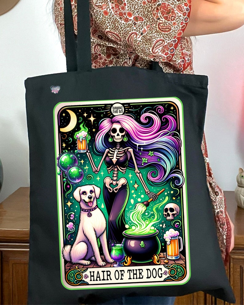May include: A black tote bag with a colorful illustration of a skeleton witch stirring a cauldron with a dog by her side. The illustration is surrounded by a green border and the text "Hair of the Dog" is at the bottom. The text "Hangover Free Kit" is at the top of the illustration.