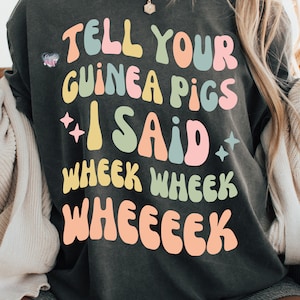 May include: A dark gray t-shirt with the text "Tell your guinea pigs I said wheek wheek wheeeek" in colorful, retro-style lettering.