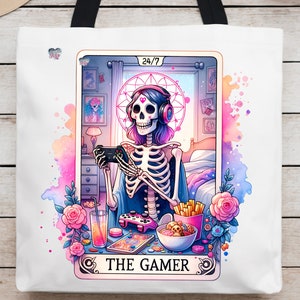 K&ouml;nnte beinhalten: Eine wei&szlig;e Einkaufstasche mit einer bunten Illustration eines Skeletts, das Videospiele spielt. Die Illustration ist im Stil einer Tarotkarte mit dem Text "The Gamer" und "24/7" auf der Karte.