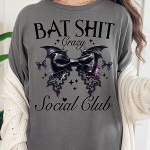 May include: Gray t-shirt with a black bat design and the text "Bat Shit Crazy Social Club".