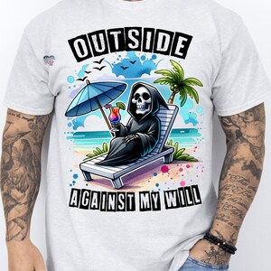 May include: A white t-shirt with a graphic of a skeleton sitting on a beach chair with a cocktail and an umbrella. The text "OUTSIDE AGAINST MY WILL" is printed on the shirt.