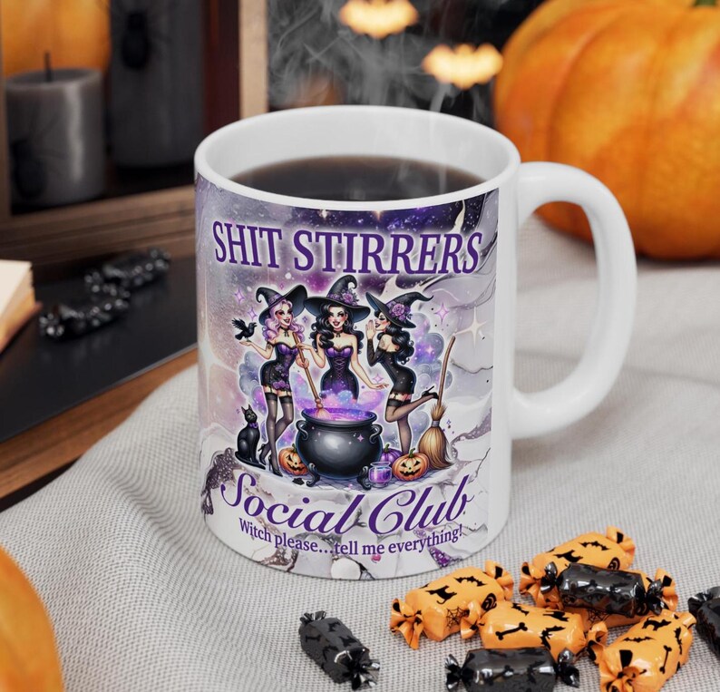 Op de afbeelding: Witte keramische mok met een paars, zwart en wit ontwerp met drie heksen die een ketel roeren. De tekst "Shit Stirrers Social Club" is op de mok gedrukt. De tekst "Witch please...tell me everything!" is onder het ontwerp gedrukt.