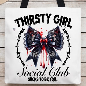May include: White tote bag with black handles. The bag has a black and red graphic of a bow with dripping blood and the text "Thirsty Girl Social Club Sucks to be you..."