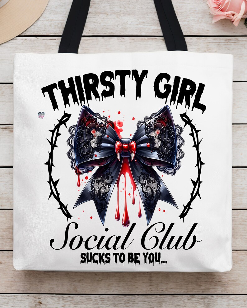 May include: White tote bag with black handles. The bag has a black and red graphic of a bow with dripping blood and the text "Thirsty Girl Social Club Sucks to be you..."