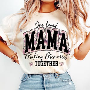 May include: A white t-shirt with a floral design and the text "One loved Mama Making Memories Together" in black.