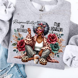May include: A grey sweatshirt featuring a graphic of a woman in a leopard print coat, striped trousers, and pink sunglasses. The text reads "Respectfully I'M RETIRED" and "NOT EXPIRED". The design includes floral elements and a coffee cup.
