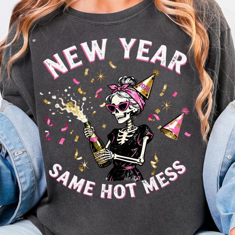 Op de afbeelding: Donkergrijze sweatshirt met de tekst "NEW YEAR SAME HOT MESS". De afbeelding toont een skelet met een zonnebril, een roze haarband en een feesthoedje, die een champagnefles opent met confetti.