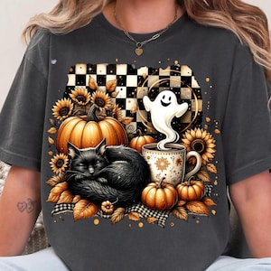 Könnte beinhalten: Dunkelgraues T-Shirt mit einem Halloween-Motiv. Das Design zeigt eine schlafende schwarze Katze, Kürbisse, Sonnenblumen, einen Geist und eine Kaffeetasse. Ein schwarz-weißes Schachbrettmuster bildet den Hintergrund.