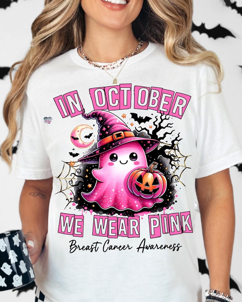 Peut inclure: T-shirt blanc avec un motif rose d'un fant&ocirc;me portant un chapeau de sorci&egrave;re et tenant une citrouille. Le texte "In October We Wear Pink" et "Breast Cancer Awareness" est imprim&eacute; en rose.