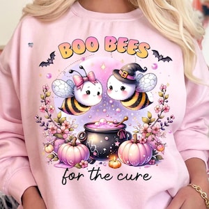 May include: Pink sweatshirt with a Halloween-themed graphic. The design features two cartoon bees, a cauldron, pumpkins, and the text "BOO BEES for the cure". Bats and floral elements complete the design.