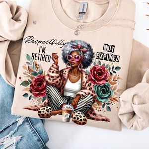 May include: Beige sweatshirt featuring a graphic of a woman in a leopard print coat, pink sunglasses, and the text "Respectfully I'm Retired Not Expired." The design includes floral elements and a coffee cup.