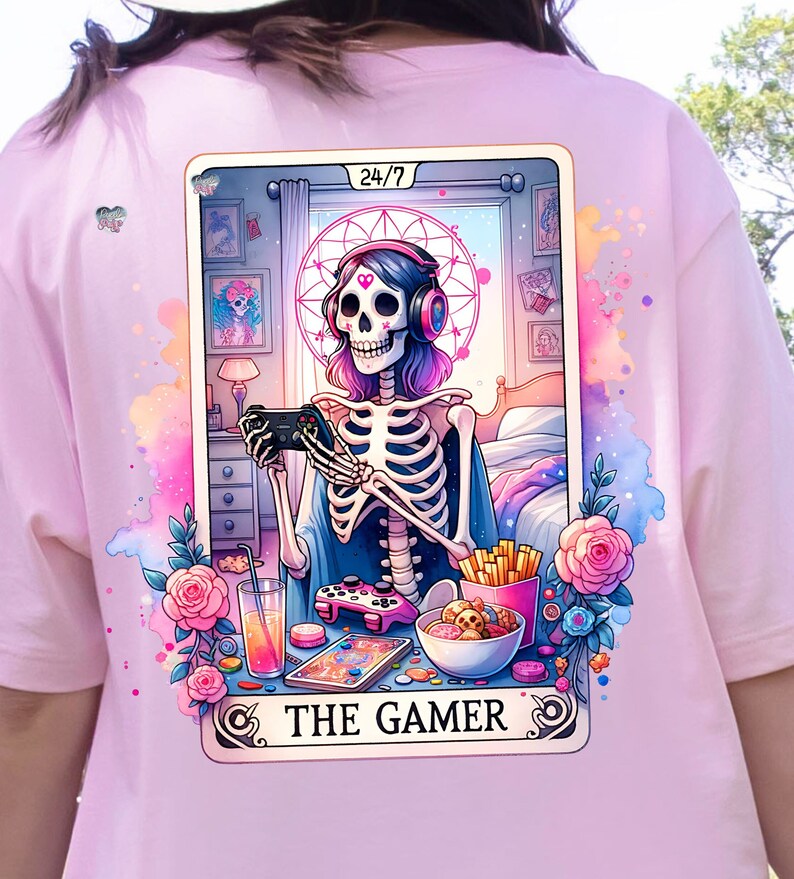 K&ouml;nnte beinhalten: Eine Tarotkarten-Illustration mit einem Skelett, das Kopfh&ouml;rer tr&auml;gt und einen Videospiel-Controller h&auml;lt. Die Karte tr&auml;gt den Titel "The Gamer" und hat ein 24/7-Symbol in der oberen rechten Ecke. Der Hintergrund ist ein rosa-blaues Aquarelldesign mit Blumen und anderen spielbezogenen Bildern.