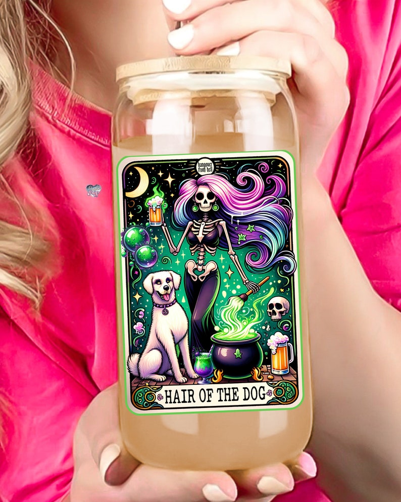 May include: A glass jar with a wooden lid and a colorful illustration of a skeleton holding a beer mug and a cauldron with green smoke. The illustration is surrounded by a green border and the text "Hair of the Dog" is at the bottom.