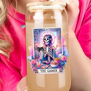 K&ouml;nnte beinhalten: Eine durchsichtige Glaswasserflasche mit einem Bambusdeckel und einem bunten Aufkleber, der ein Skelett zeigt, das Videospiele spielt. Der Aufkleber lautet "24/7 The Gamer".