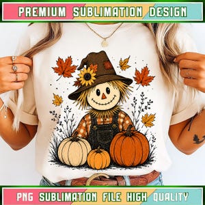 Puede incluir: Una camiseta color crema con un gráfico de un espantapájaros con sombrero y girasol, camisa de cuadros y peto, rodeado de calabazas y hojas de otoño. El texto "PREMIUM SUBLIMATION DESIGN" y "PNG SUBLIMATION FILE HIGH QUALITY" aparece en la parte superior e inferior.