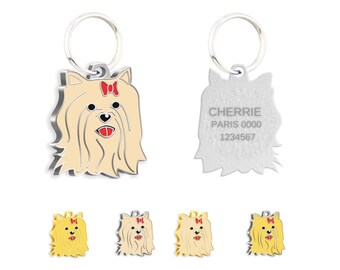 Puede incluir: Placa de identificación para perros con diseño de Yorkshire Terrier. La parte delantera presenta un perro beige con un lazo rojo. La parte trasera está grabada con "CHERRIE", "PARIS 0000" y un número de teléfono. Se muestran etiquetas adicionales en oro y plata.