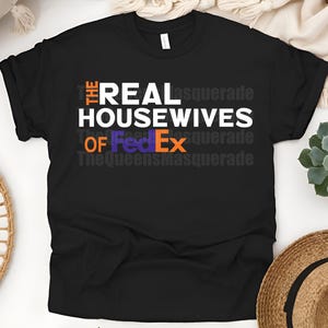 May include: Black t-shirt with the text "THE REAL HOUSEWIVES OF FedEx" in white, orange, and purple. The shirt also has the text "TheQueensmasquerade" in a faded gray font.