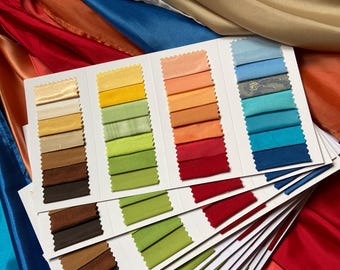 May include: A fabric swatch sample card featuring multiple rows of small, rectangular fabric pieces in a wide spectrum of colors including yellow, orange, red, green, blue, and brown, arranged against a background of draped, colorful satin fabric.