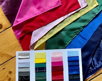 May include: A collection of layered, multi-colored satin fabric swatches in shades of purple, pink, red, light pink, yellow, green, blue, and navy. A white display card features four columns of smaller fabric samples in various colors and textures.