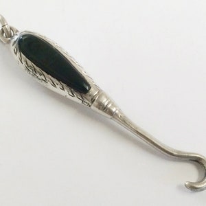 May include: A silver and black hook with an ornate design. The hook has a black stone set into the handle.