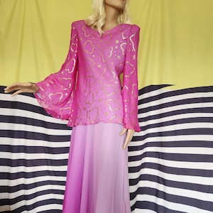 Puede incluir: Conjunto vintage de dos piezas rosa sobre un maniquí. La parte superior tiene mangas largas y acampanadas y un estampado dorado. La falda es un degradado de tonos rosas. El conjunto se exhibe sobre un fondo a rayas amarillas y negras.
