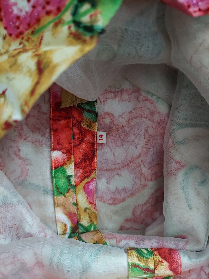 Op de afbeelding: Close-up van de binnenkant van een jurk met bloemenprint en een rode, groene en gouden bies. Het maatlabel geeft "14" aan.